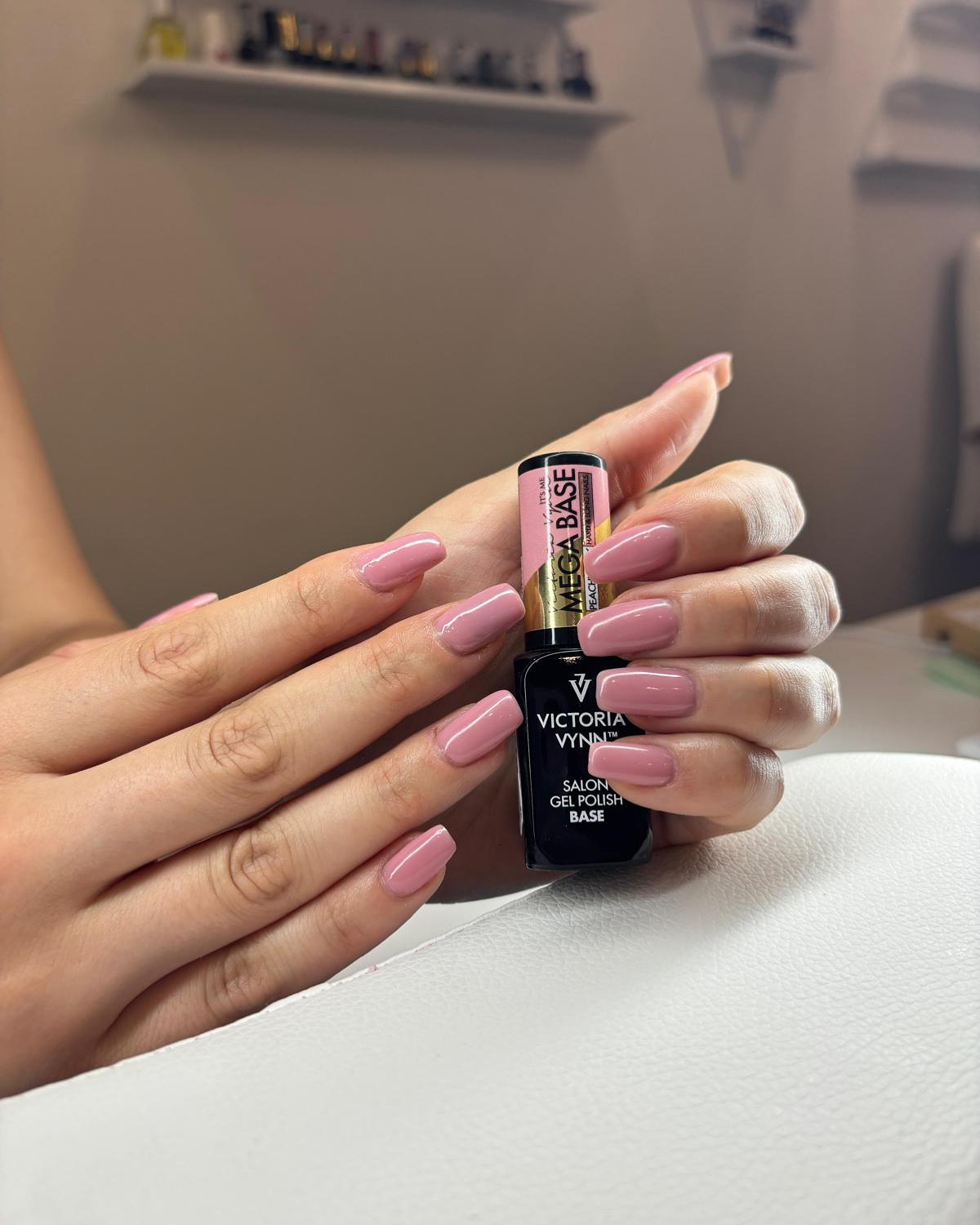 Gemanicuurde nagels in zacht roze gellak, naast een flesje basecoat