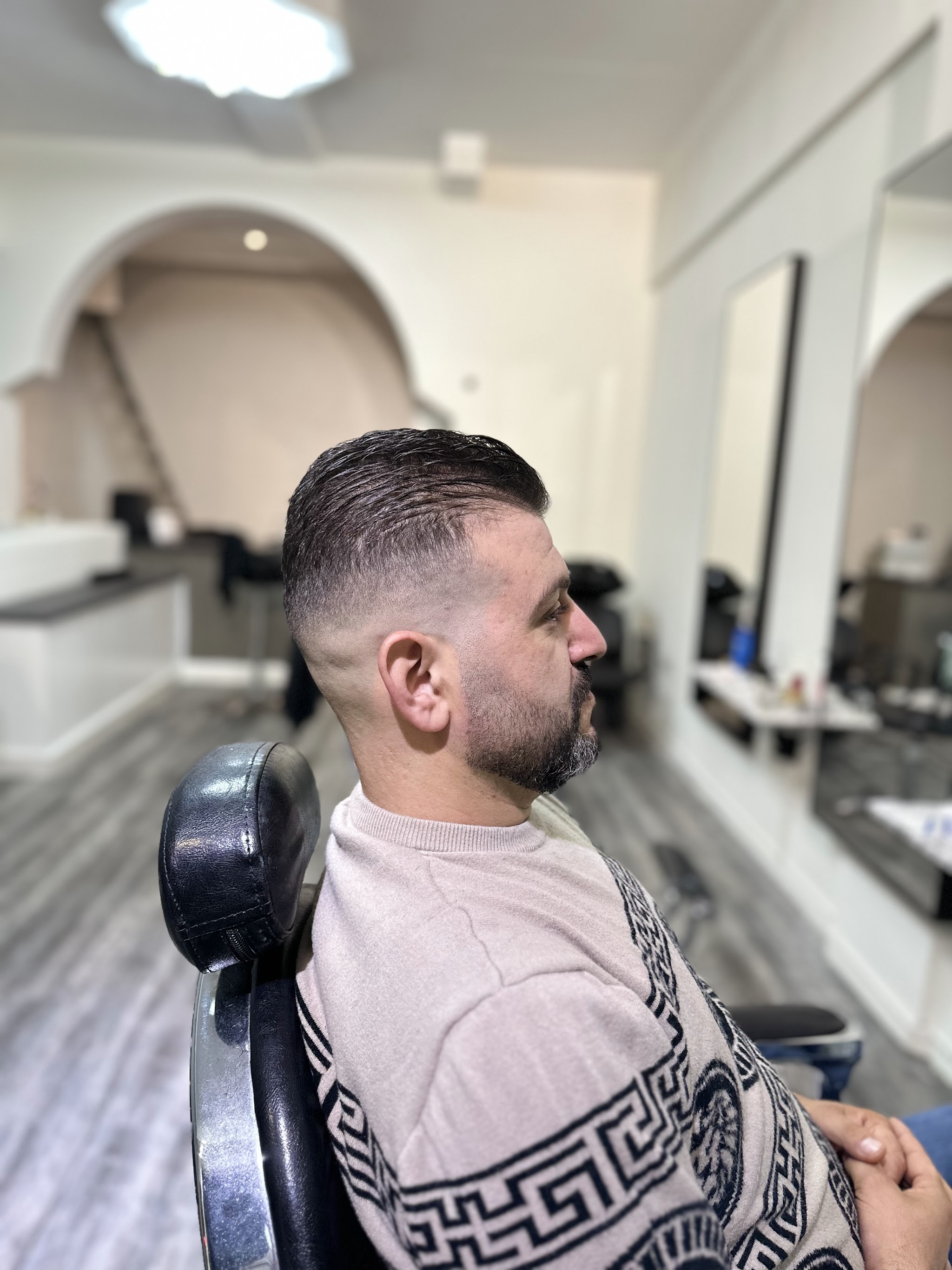 Klant in de stoel met een strakke fade en verzorgde baard, van opzij