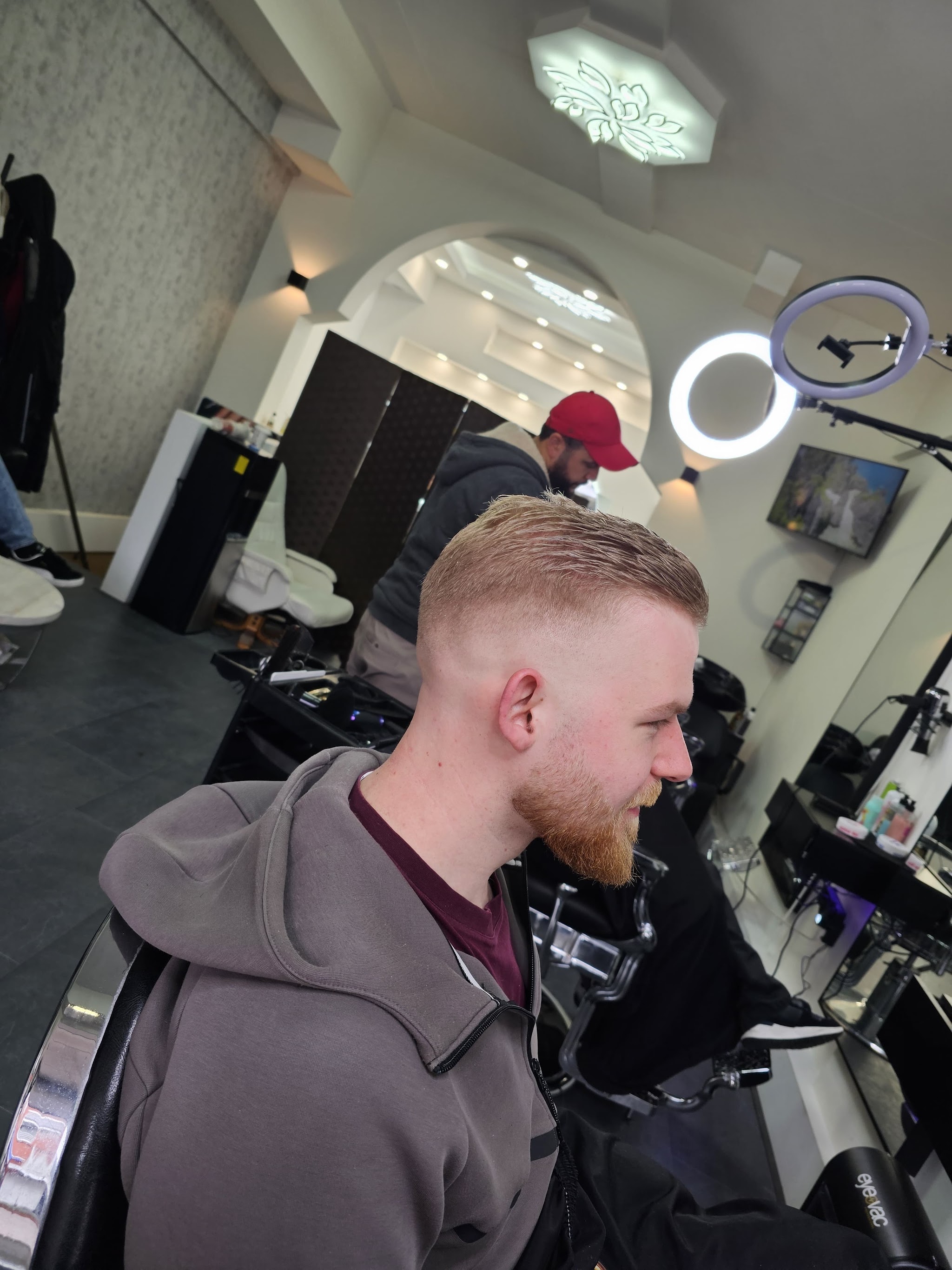 Een klant met een korte fade in de kappersstoel, met de bogen en spiegels van de salon op de achtergrond