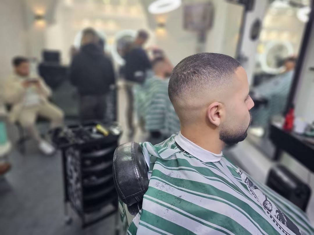 Klant in een groen-wit gestreepte kapmantel met een korte fade